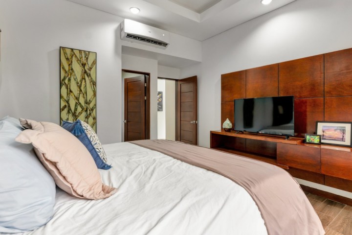 Modern bedroom with bed, TV, and wooden decor on wall.