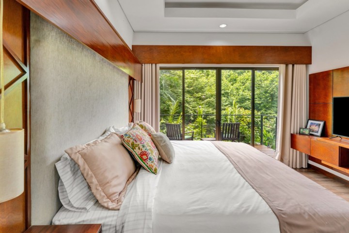 Modern bedroom with large bed, sliding glass doors to balcony, and view of lush greenery.