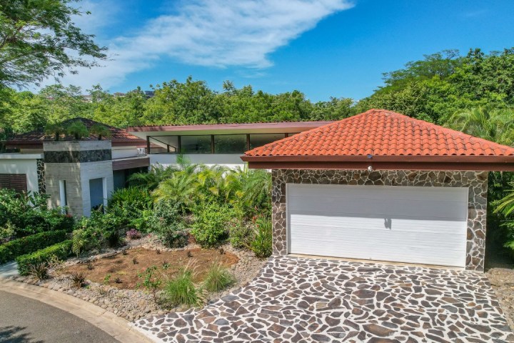 Modern house with stone and tile exterior, surrounded by lush greenery.