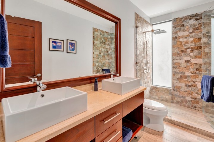 Modern bathroom with twin sinks, stone shower wall, and wood accents.