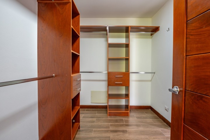 Wooden walk-in closet with shelves and hanging rods on a tiled floor.