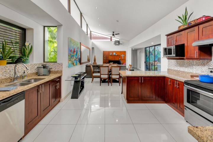Modern kitchen with wood cabinets, plants, and dining area in background, featuring stainless steel appliances.