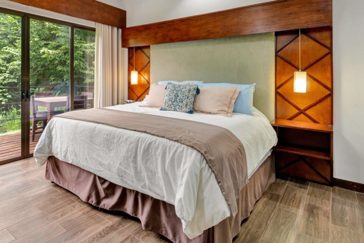 Bedroom with a large bed, wooden accents, pendant lights, and a balcony view of trees.