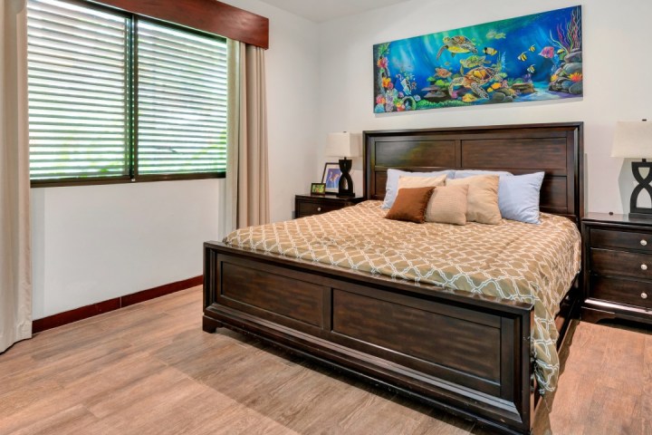 Bedroom with wooden bed, beige bedding, ocean artwork, side tables, and lamps.
