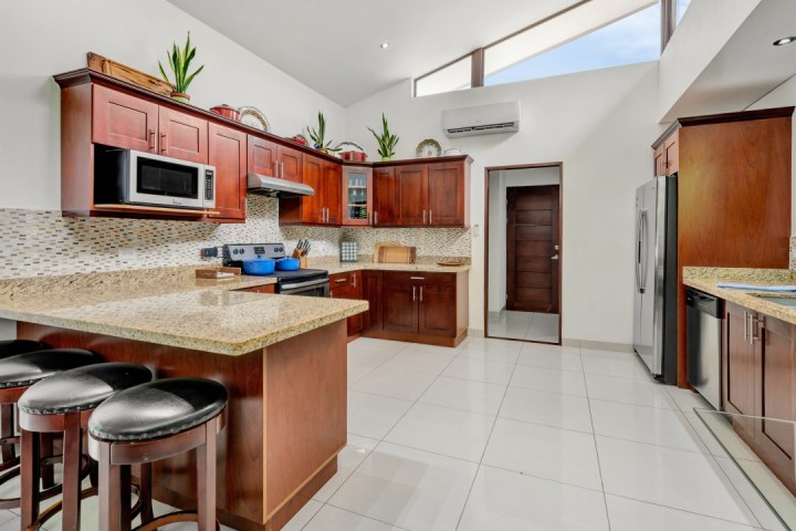 Modern kitchen with wooden cabinets, island, stainless appliances, and bar stools.