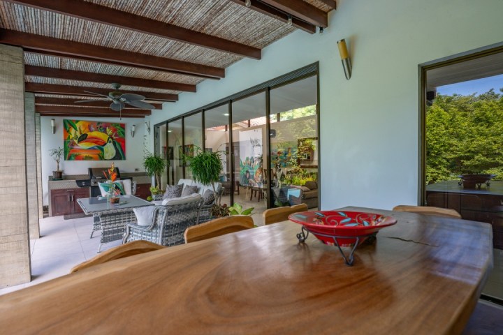 Outdoor patio with wooden table, art, wicker chairs, plants, and glass doors.