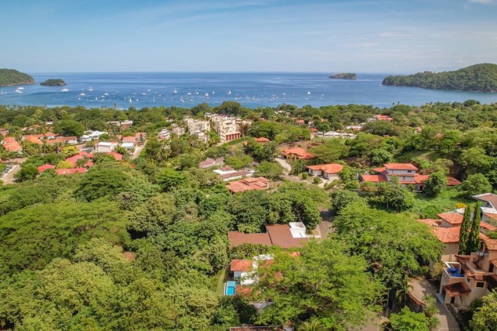 Aerial view of a coastal town with lush greenery, buildings, and boats in the bay.