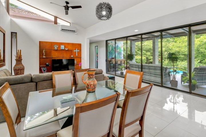 Modern living and dining area with glass doors opening to a patio and greenery outside.