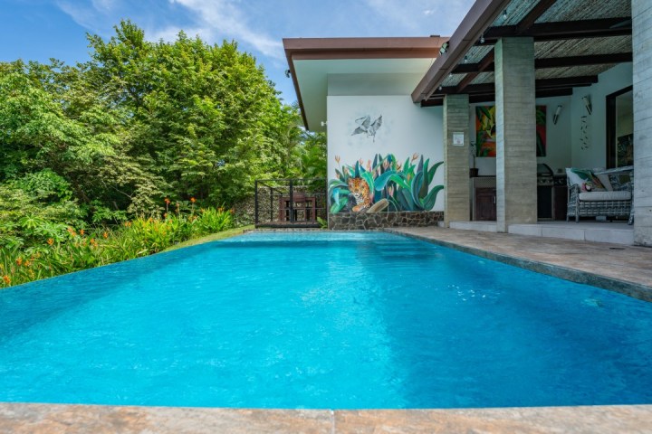 Poolside view with mural of a jaguar, surrounded by lush green trees and open patio.