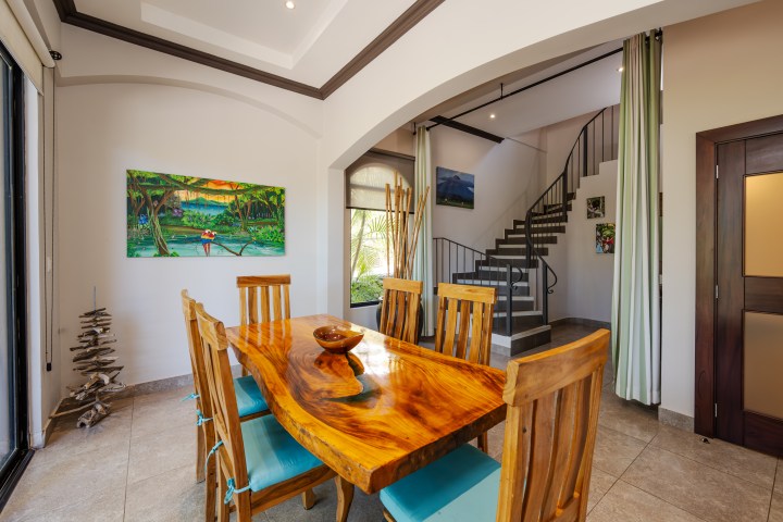 Modern dining room with wooden table and chairs, wall art, and staircase in background.