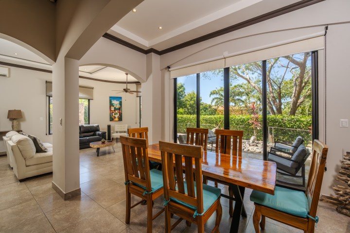 Modern dining area with large windows overlooking a garden, adjacent to a living room with sofas.