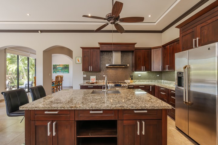 Modern kitchen with granite countertops, wooden cabinets, ceiling fan, and stainless steel appliances.