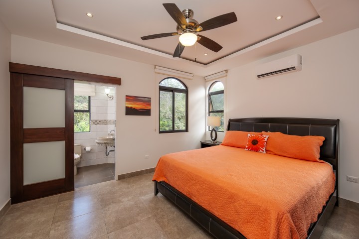 Bedroom with orange bedding, ceiling fan, and attached bathroom with sliding door.