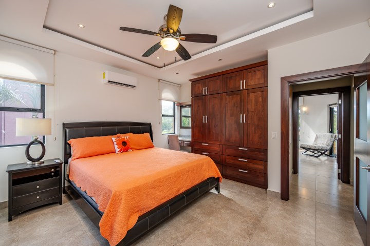 Bedroom with orange bedding, ceiling fan, wooden wardrobe, and two windows.