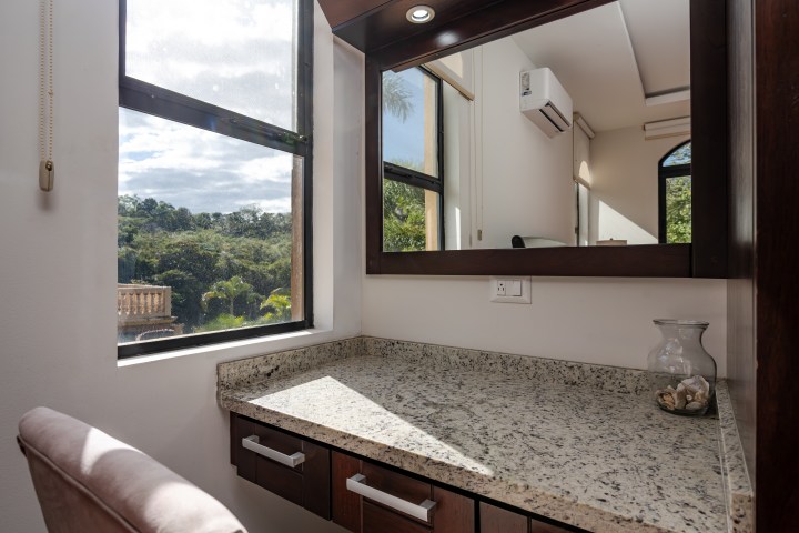 A granite-topped vanity with a mirror and chair by a window showing an outdoor view.