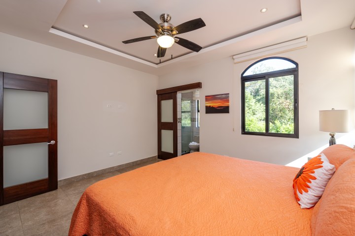 Bedroom with orange bedding, ceiling fan, arched window, and wooden doors.