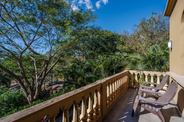 Balcony with two chairs and a view of trees and blue sky.
