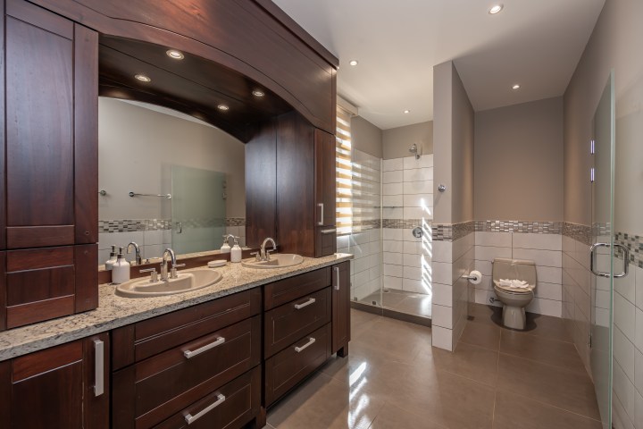 Modern bathroom with dark wood cabinets, dual sinks, and a glass shower.