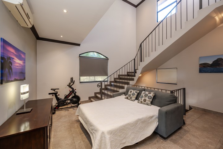 Room with exercise bike, staircase, bed, and artwork on walls.