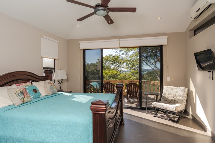 Bedroom with a large bed, ceiling fan, and sliding glass doors opening to a balcony with outdoor seating.