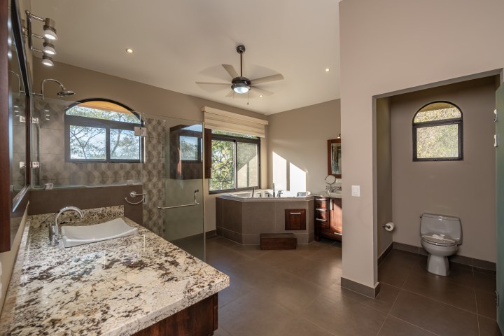 Modern bathroom with granite countertops, corner bathtub, and separate toilet area.