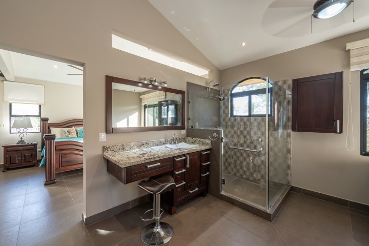 Modern bathroom with glass shower, granite countertop sink, and open doorway to bedroom.