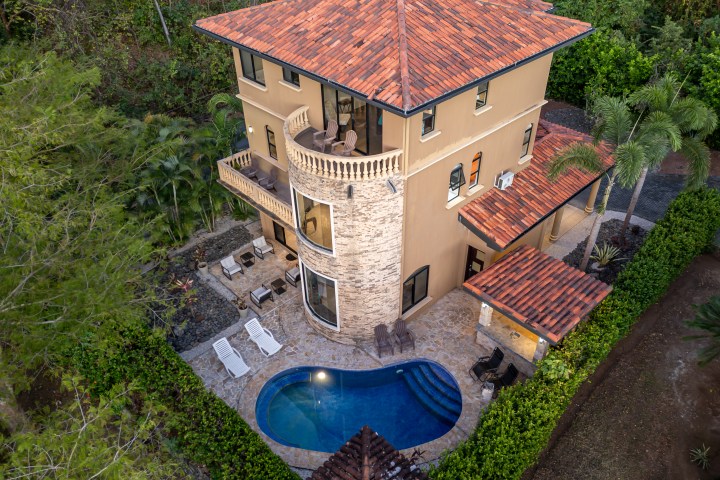 Aerial view of a three-story house with a pool, surrounded by trees.