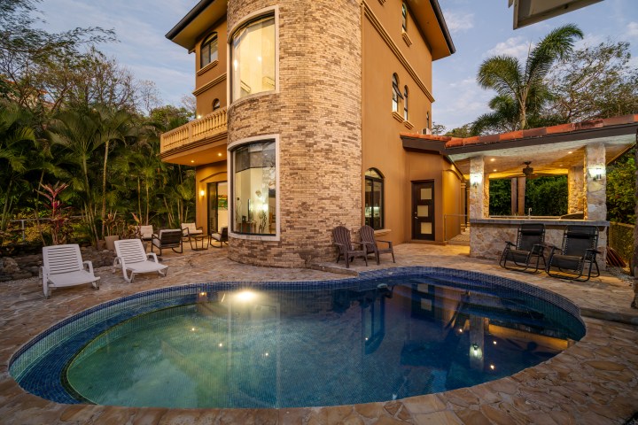 A luxury house with a pool and patio surrounded by tropical plants.