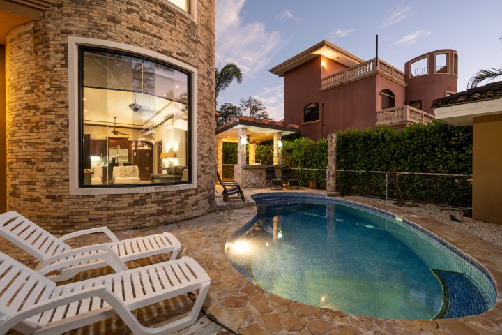 Garden view of a house with swimming pool and lounge chairs at twilight.