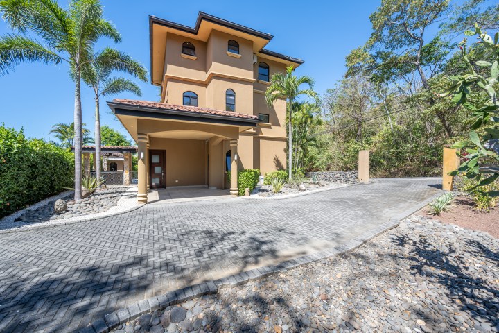Three-story tan house with palm trees and a stone driveway.