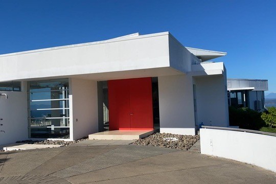 Modern white house with red door and glass panels under a clear blue sky.