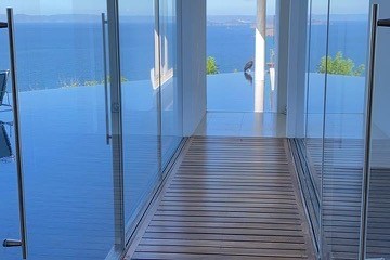 Glass walkway with wooden floor offers ocean view through windows on both sides.