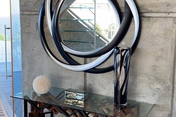 Modern mirror and console table with decorative items against a concrete wall.