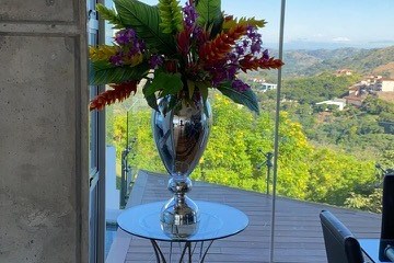 Vase with colorful flowers on table, glass doors revealing scenic mountain view.