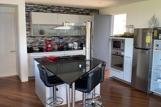 Modern kitchen with island, bar stools, stainless appliances, and mosaic tile backsplash.