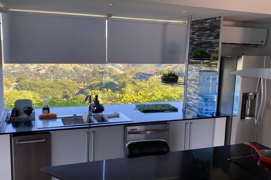 Modern kitchen with black countertops, large windows, and a scenic view of hills.