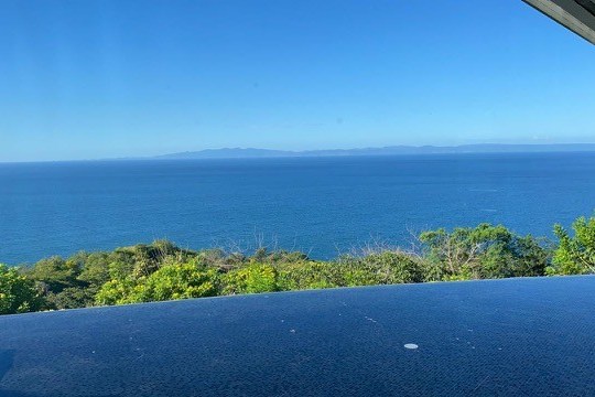 Infinity pool overlooking ocean with distant land and clear blue sky.