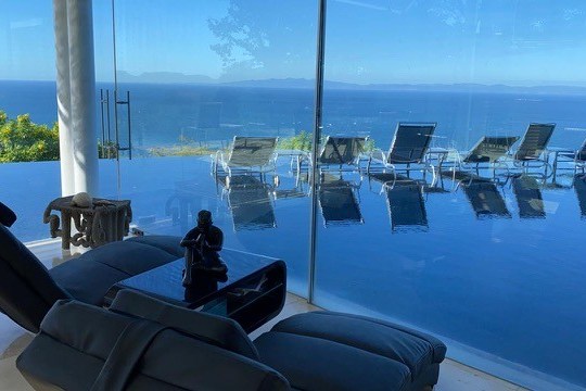 Lounge chairs by an infinity pool with ocean view through glass walls.