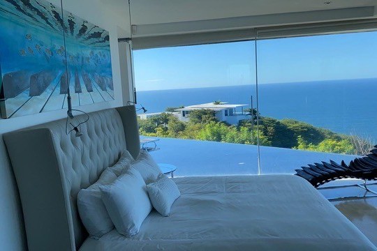 Bedroom with ocean view, large window, bed, and modern chair.