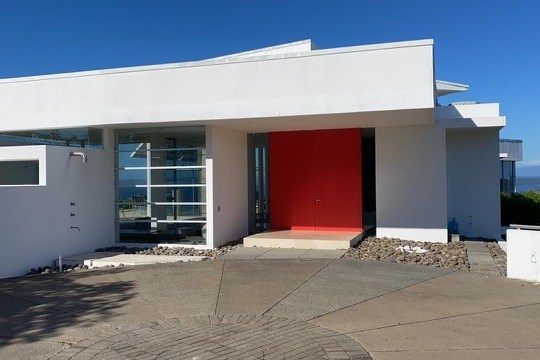 Modern house with white walls, red door, and ocean view in background.