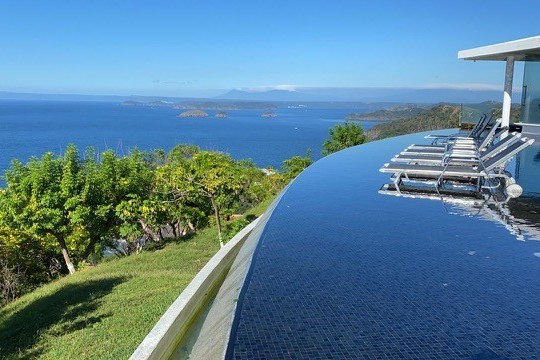 Infinity pool with lounge chairs overlooks ocean and islands on a clear day.