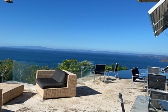 Outdoor patio with wicker furniture overlooking a blue sea and distant mountains under clear sky.