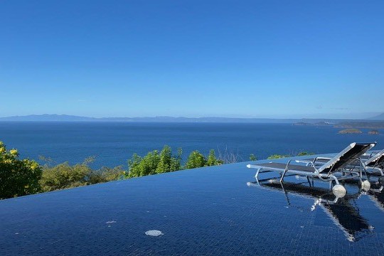 Infinity pool with loungers, ocean view, and clear blue sky.