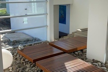 Modern indoor walkway with wooden slats over river stones, surrounded by glass walls.