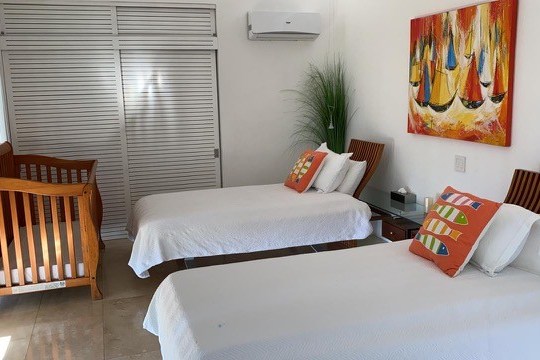 Room with two beds, a crib, colorful pillows, and a painting of sailboats.