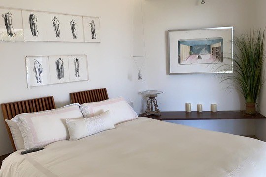 Modern bedroom with artwork, wooden headboard, white bedding, and decorative items.