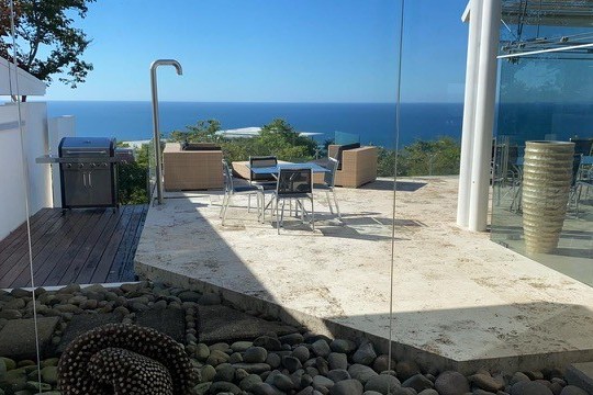 Modern terrace with seating, grill, ocean view, and decorative stones.