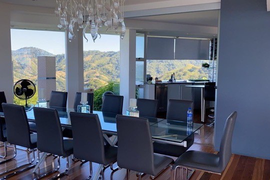 Modern dining room with glass table, black chairs, and mountain view.