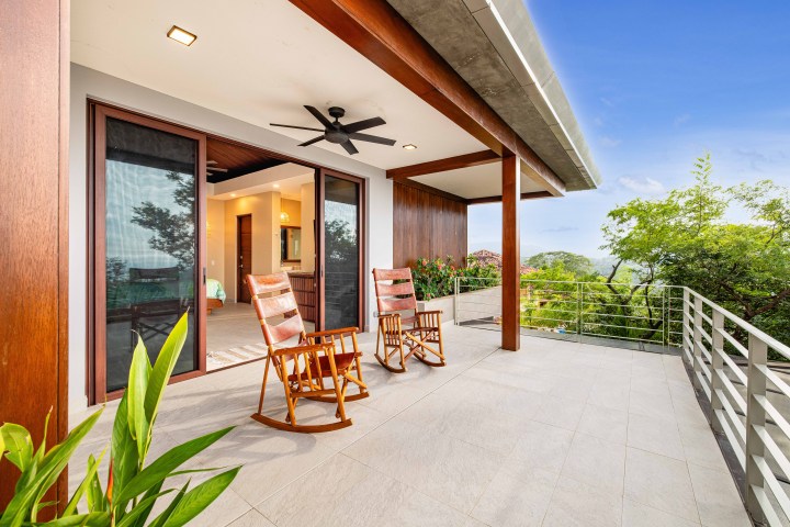 Outdoor patio with two wooden rocking chairs, sliding glass doors, ceiling fan, and forest view.