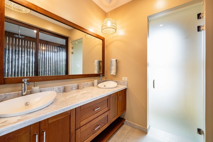 Bathroom with double sinks, wooden cabinets, large mirror, and frosted glass door.